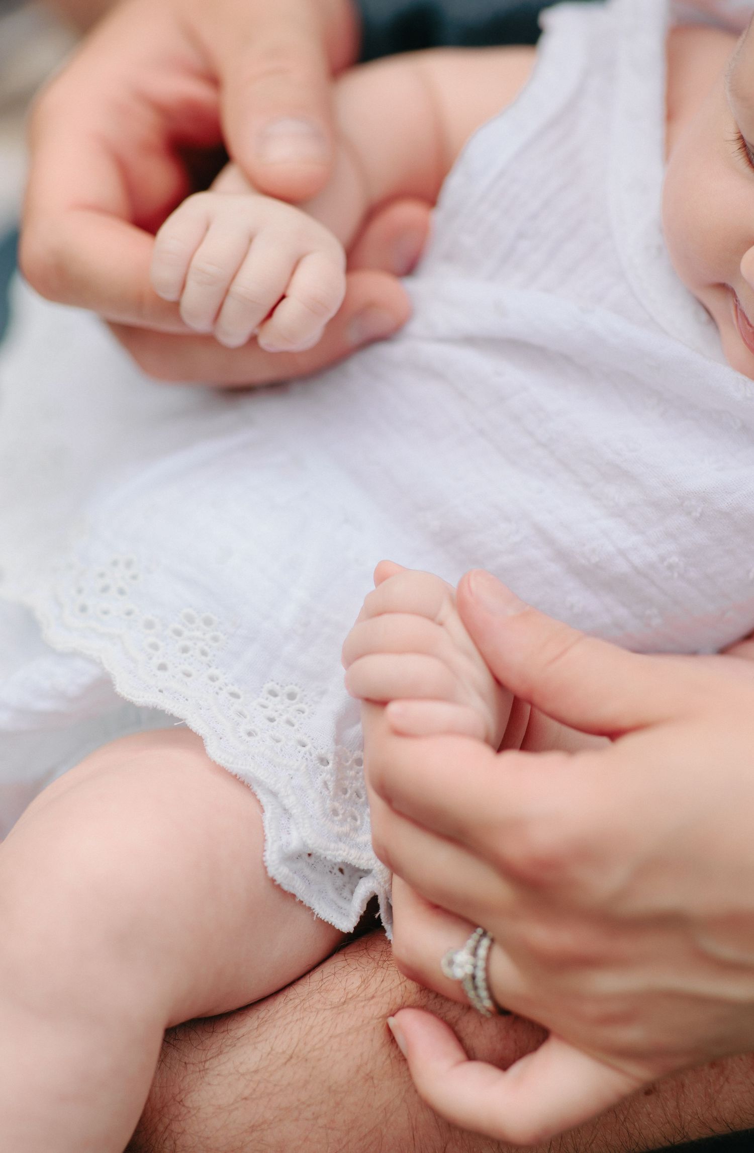 Close-up view of tiny baby hands grasping while wearing white lace clothing.