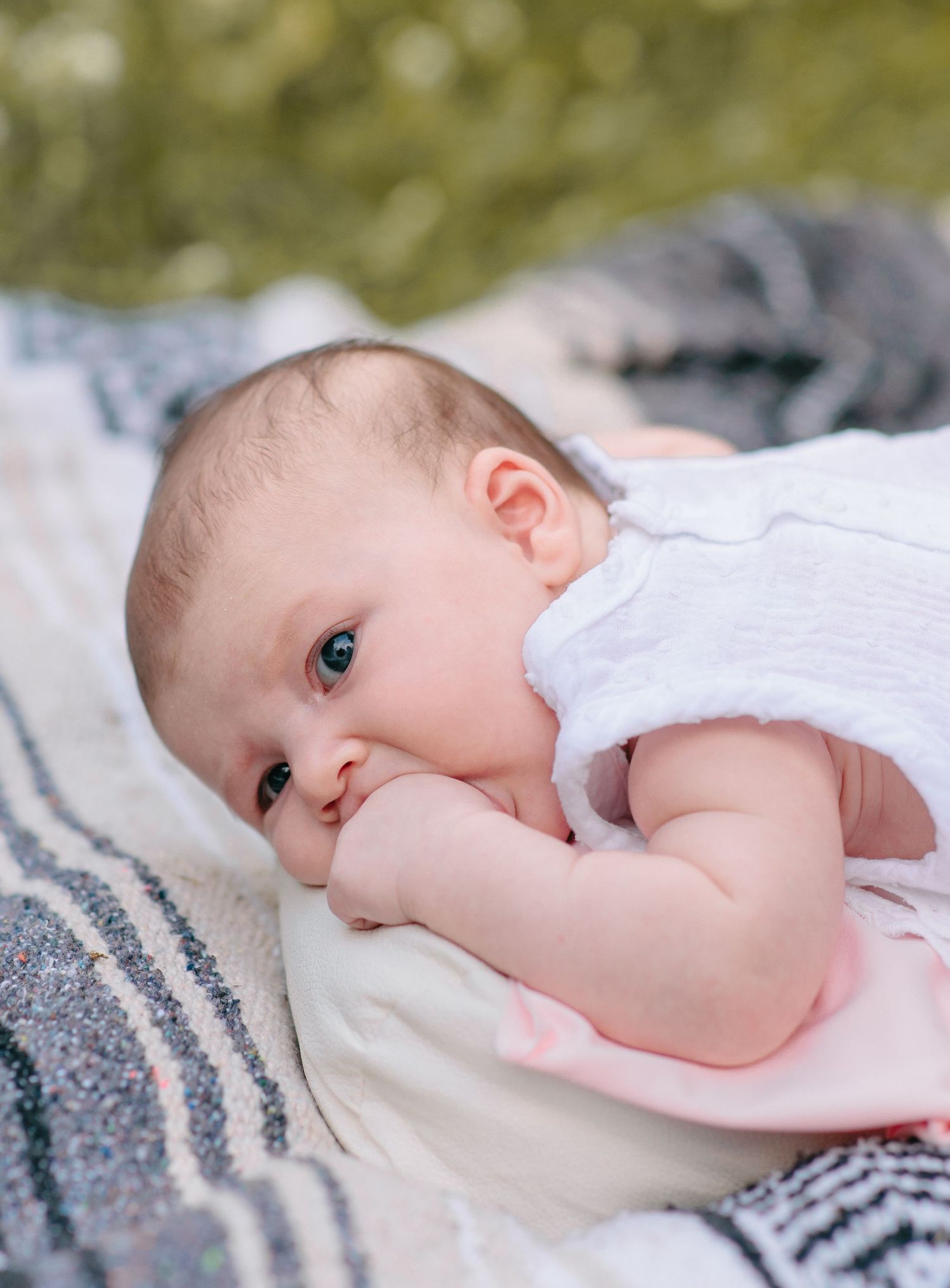 Baby lies on a striped blanket looking at the camera with bright eyes in natural light.