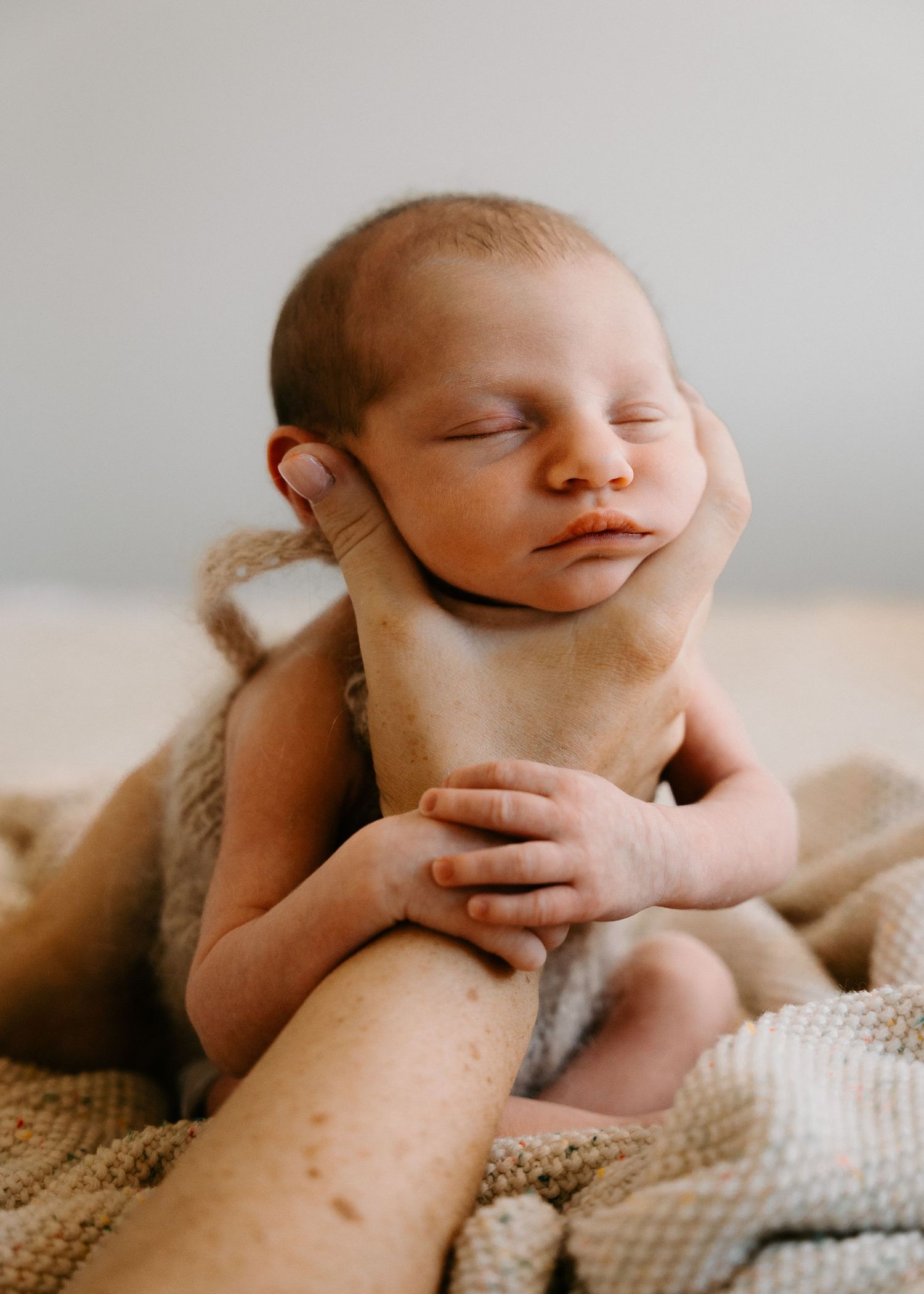 A peaceful sleeping newborn baby posed on soft brown fabric.
