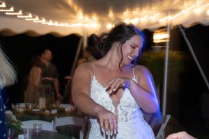 Someone in a white lace wedding dress dances joyfully under string lights at an outdoor evening reception.