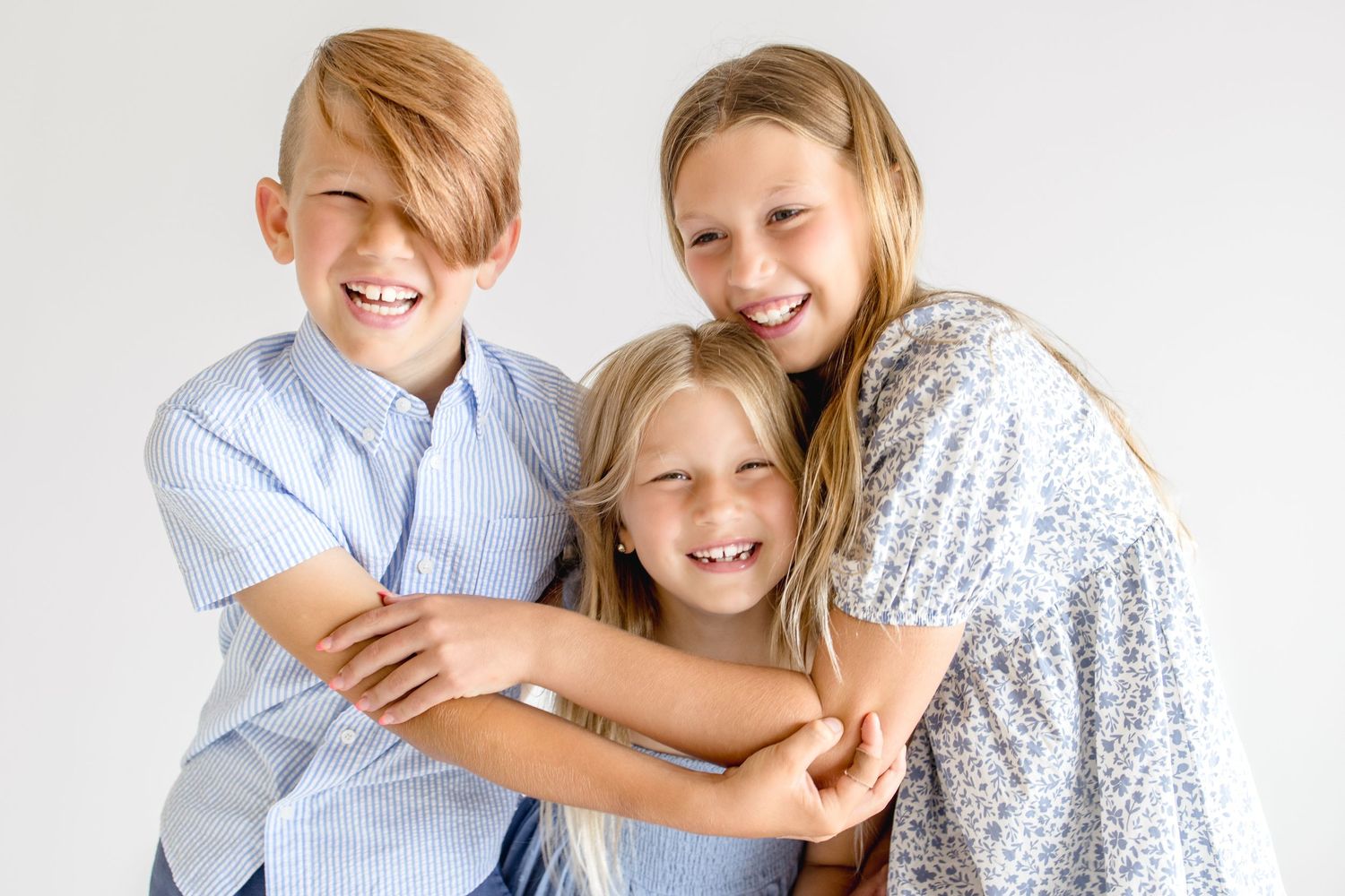Three people share a joyful embrace while wearing coordinated blue and white outfits against a white background.