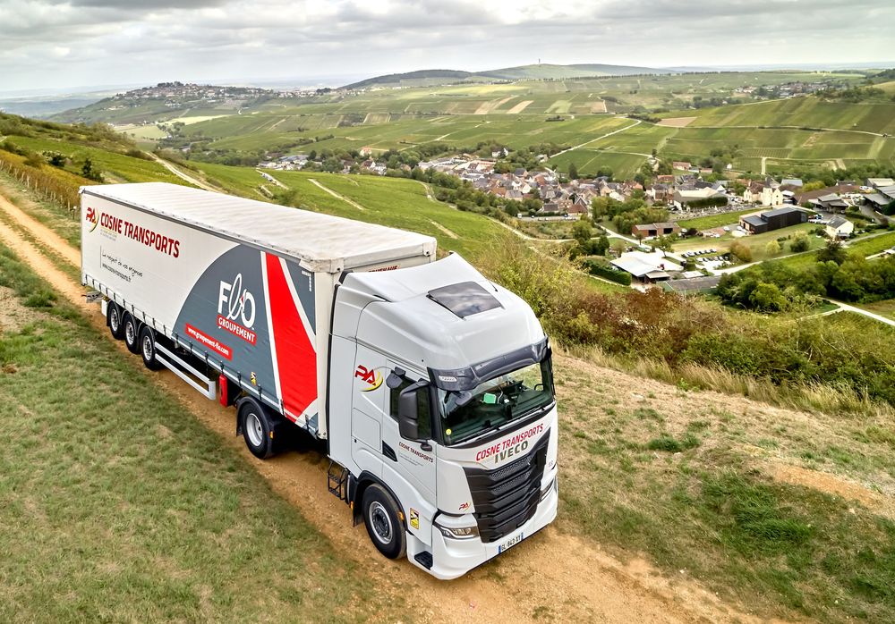 Fleet of branded semi trucks traveling through hilly countryside on winding roads.