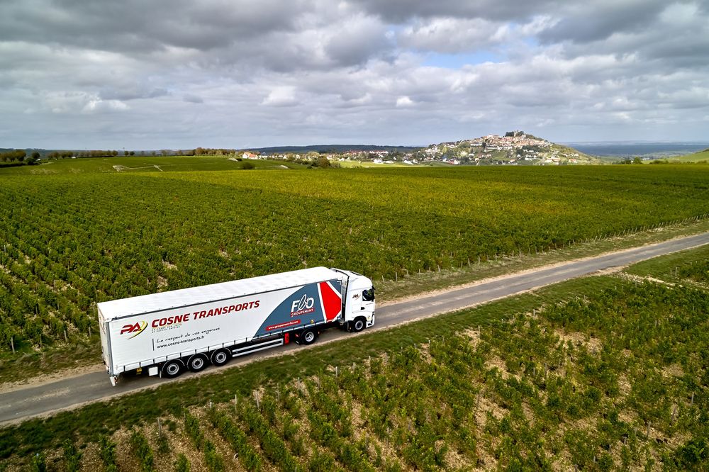 Semi-remorques traversant des vignobles pittoresques sous un ciel nuageux.