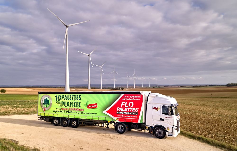 Grand camion commerciaL et des éoliennes le long d'une route rurale sous un ciel nuageux.