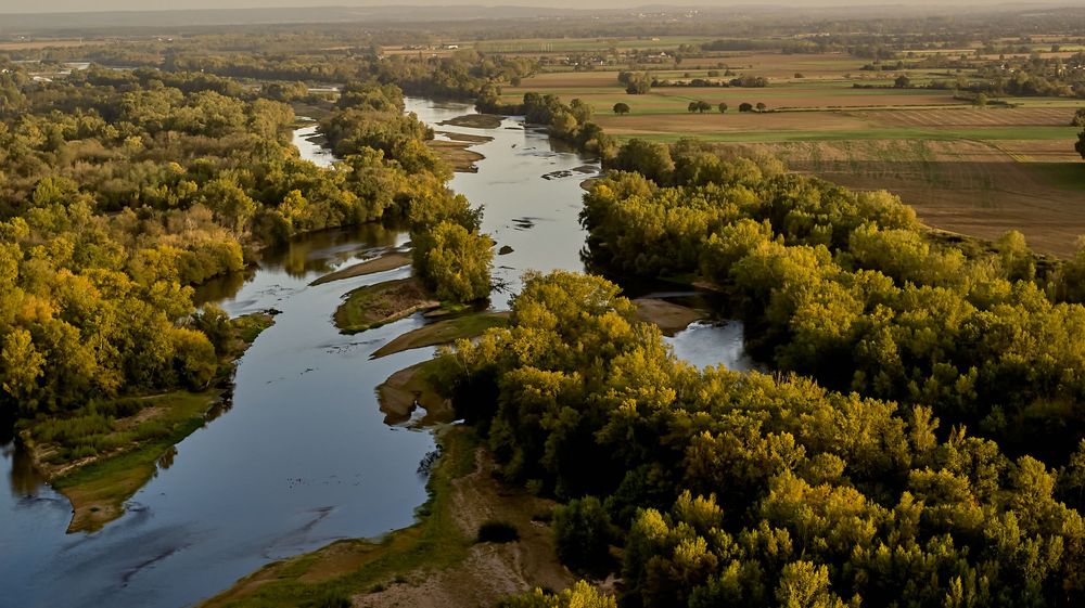 Rivière pittoresque serpente à travers les champs agricoles et les collines au coucher du soleil.
