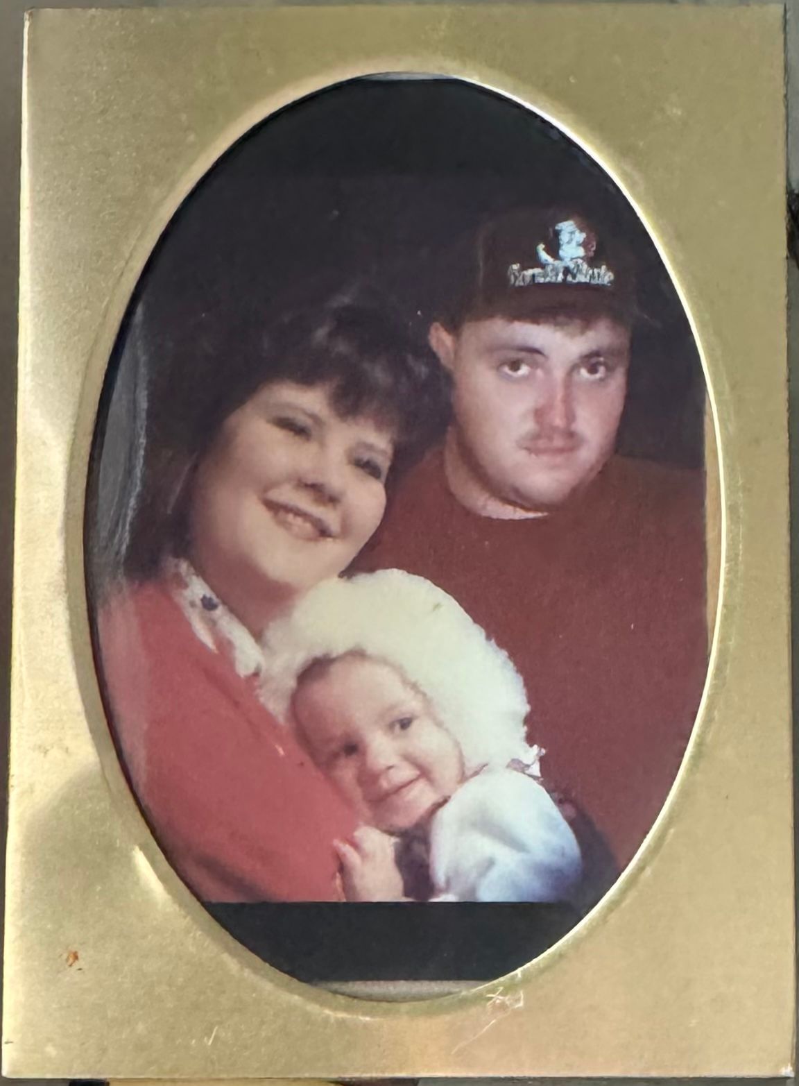 A vintage oval-framed family portrait photograph with three people in red and white against a dark background.