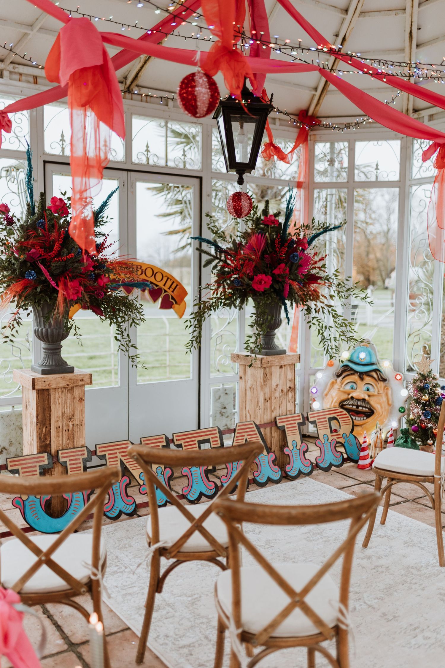 Elegant glass conservatory decorated with red ribbons, floral arrangements and wooden director chairs for a special event.