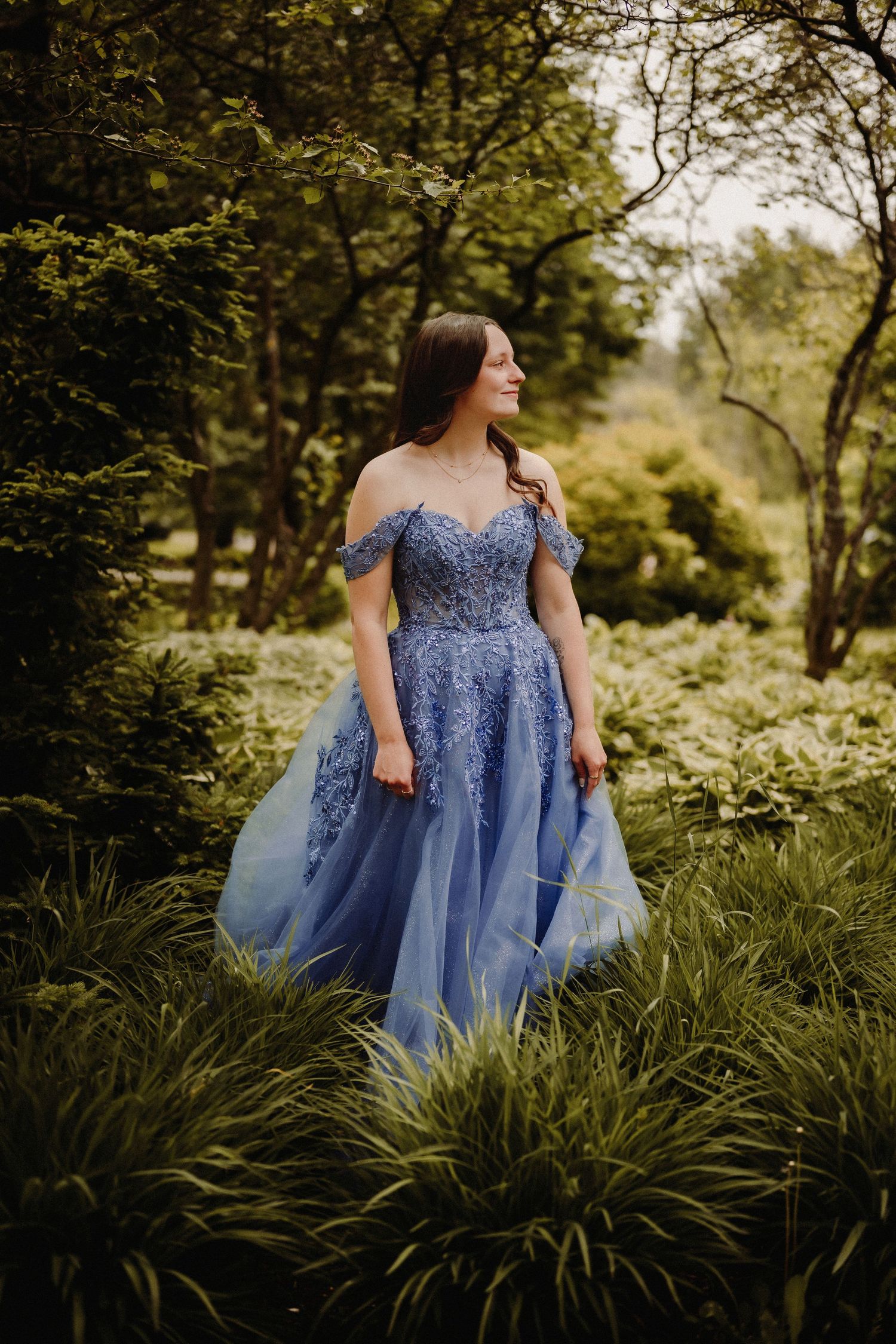 A blue tulle ball gown with off-shoulder detail sparkles in an enchanted forest setting during golden hour.
