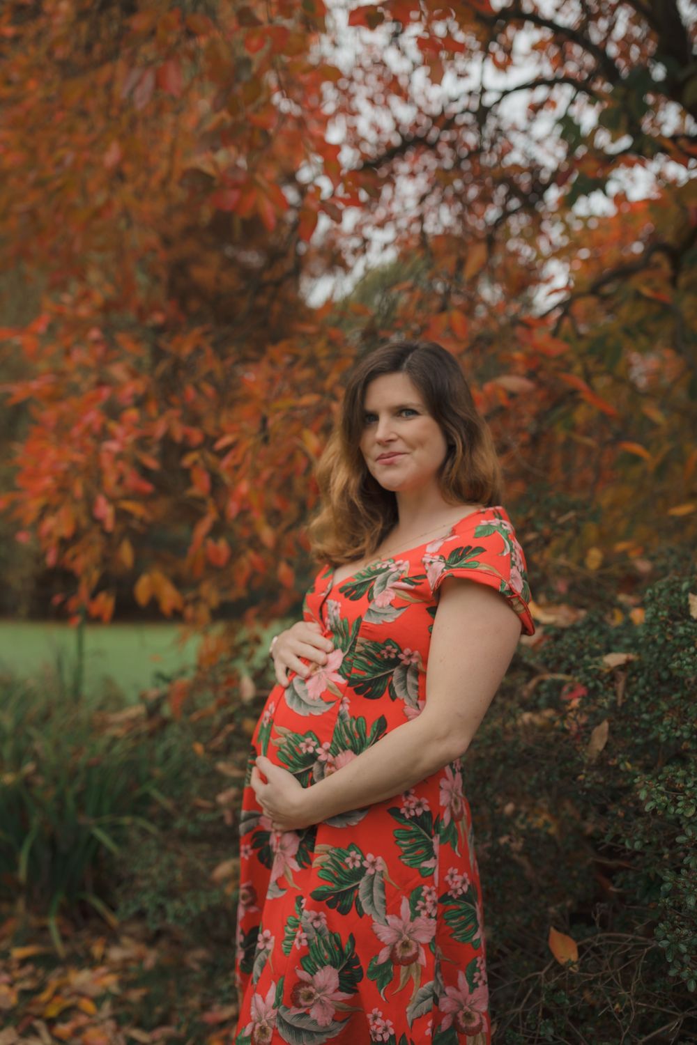 Person in floral red dress poses against vibrant autumn foliage backdrop.