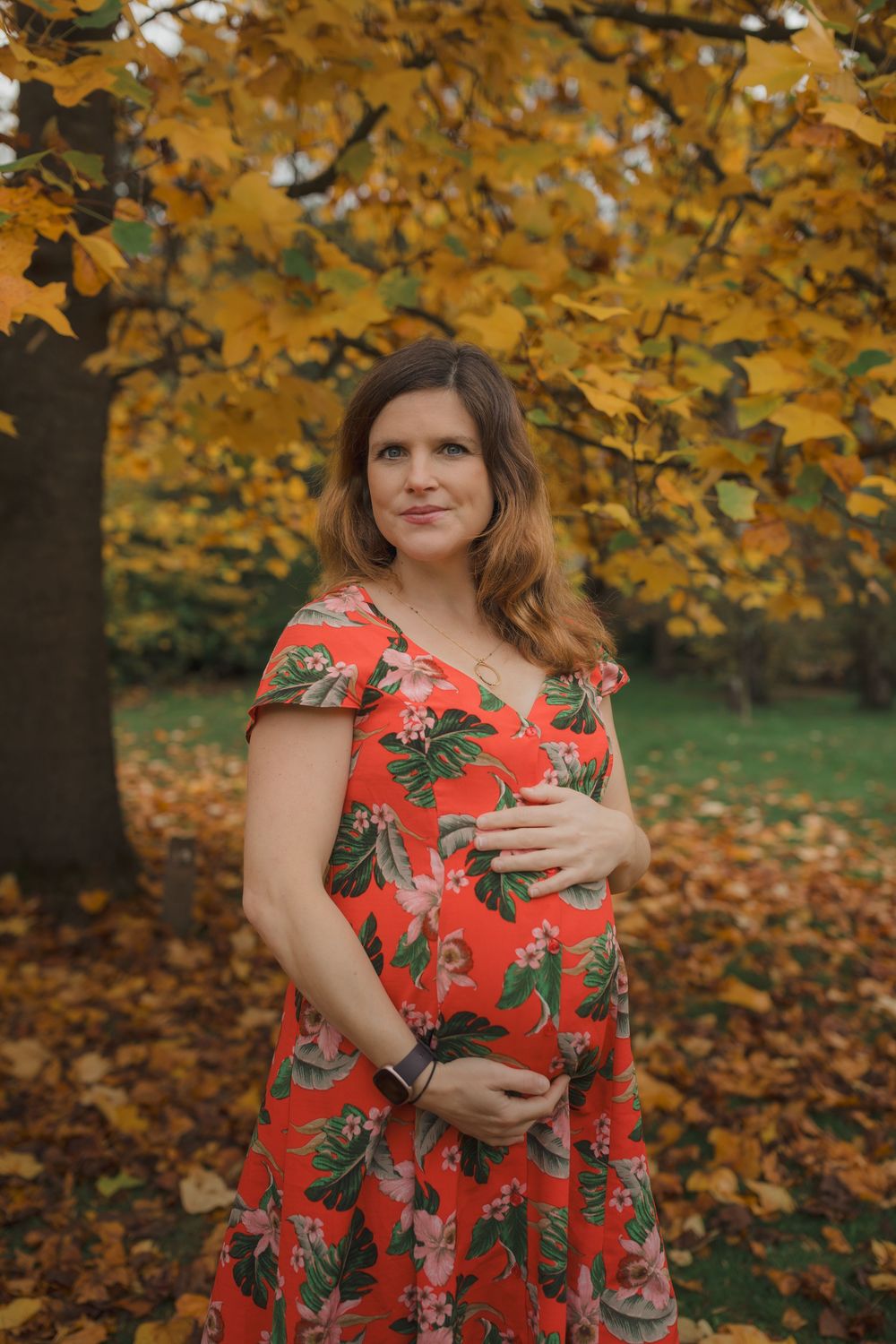 Fall photoshoot featuring someone in a bright coral floral dress among golden autumn leaves.