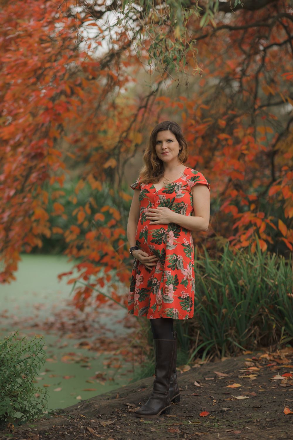 Portrait session in autumn setting with person wearing red floral dress against colorful fall foliage.