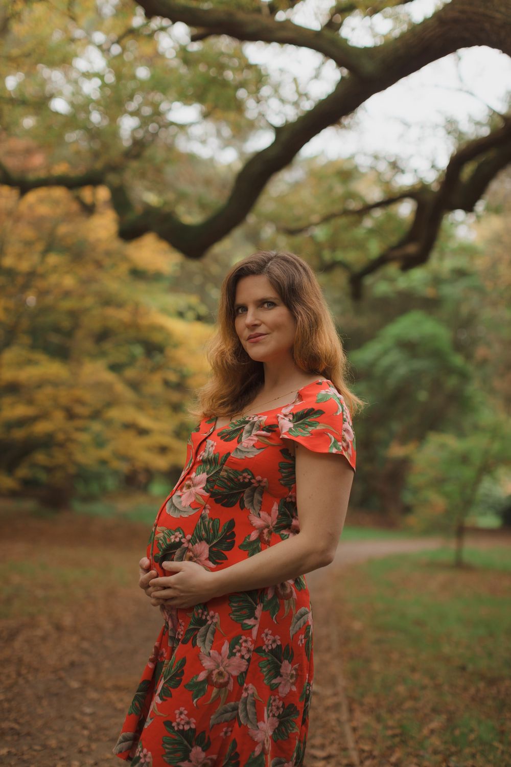 Orange and red autumn leaves frame scene with red floral dress in garden setting.