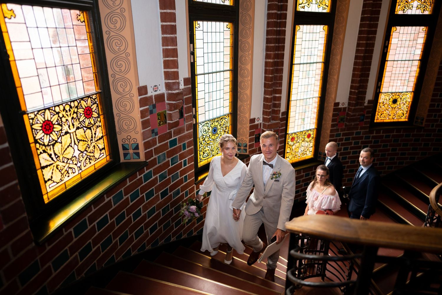 Hochzeitsfotograf Schloss Köpenick Berlin – Brautpaar läuft Hand in Hand Treppe mit bunten Fenstern hinauf