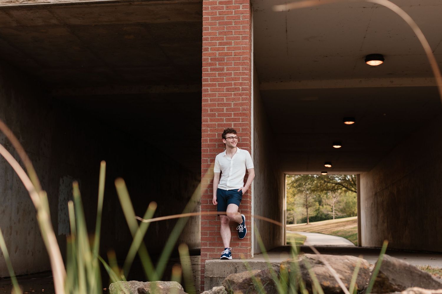 Modern brick underpass with natural landscaping elements creates an urban backdrop for this senior boy.