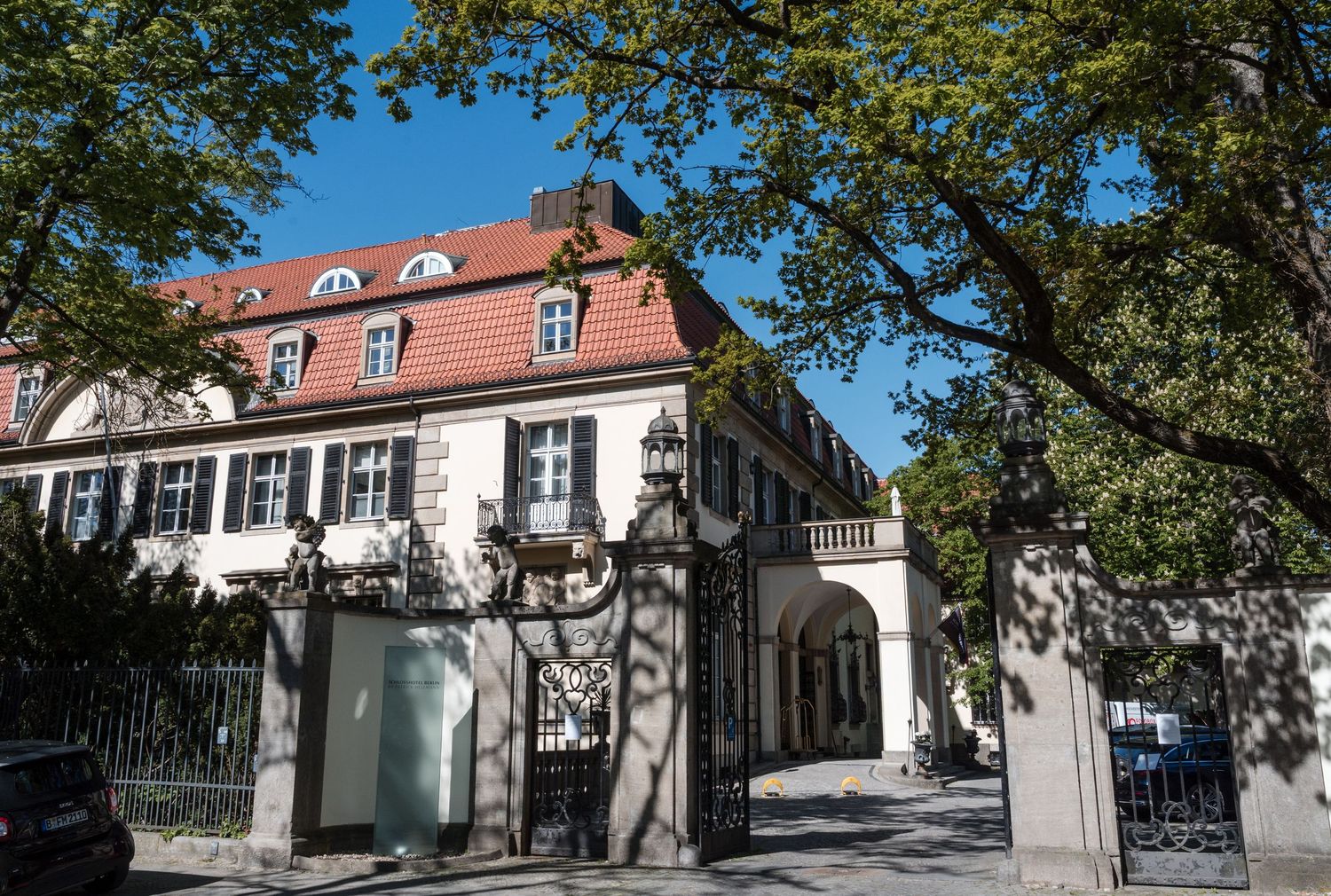 Historic white mansion buildings with classical architecture line a shaded street in a scenic European neighborhood.