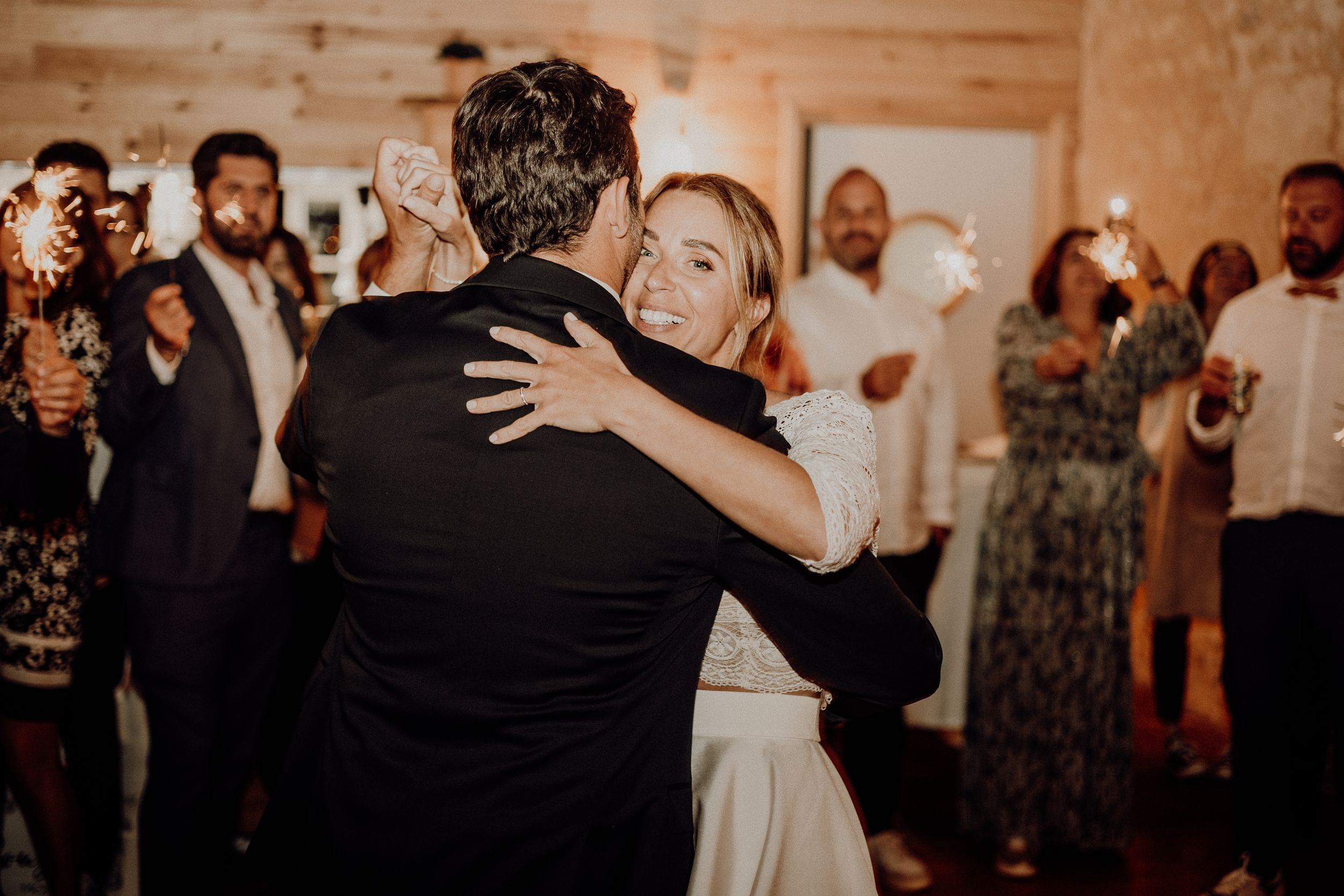 A bride and groom share their first dance surrounded by guests holding sparklers at a wedding reception.