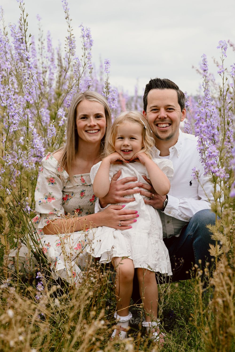 Family poses together in a field of blooming purple wildflowers at the confetti fields on a cloudy day.