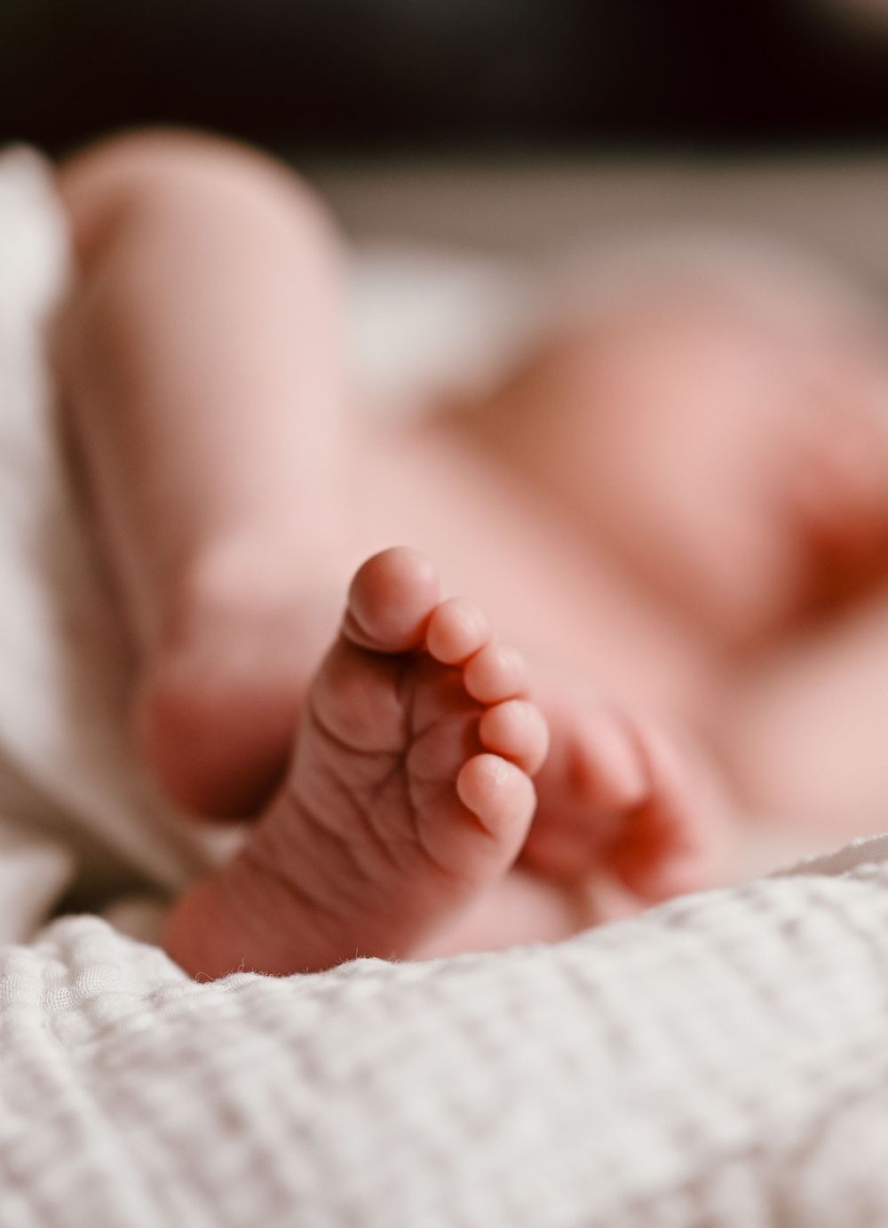 Close-up photo of a tiny baby foot resting on soft white textured fabric with shallow depth of field.