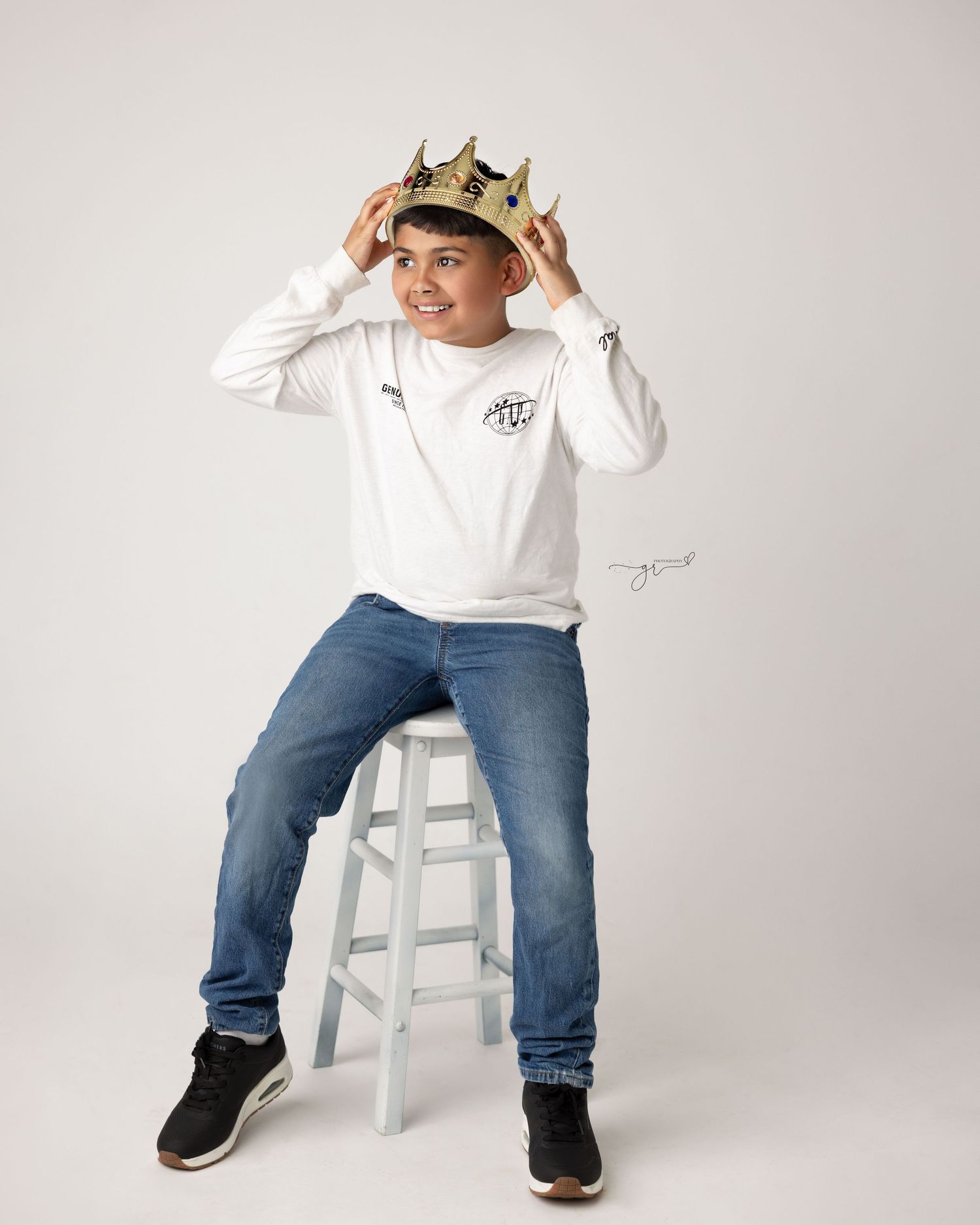 A joyful moment captured wearing a gold crown and white sweatshirt while sitting on a white stool.
