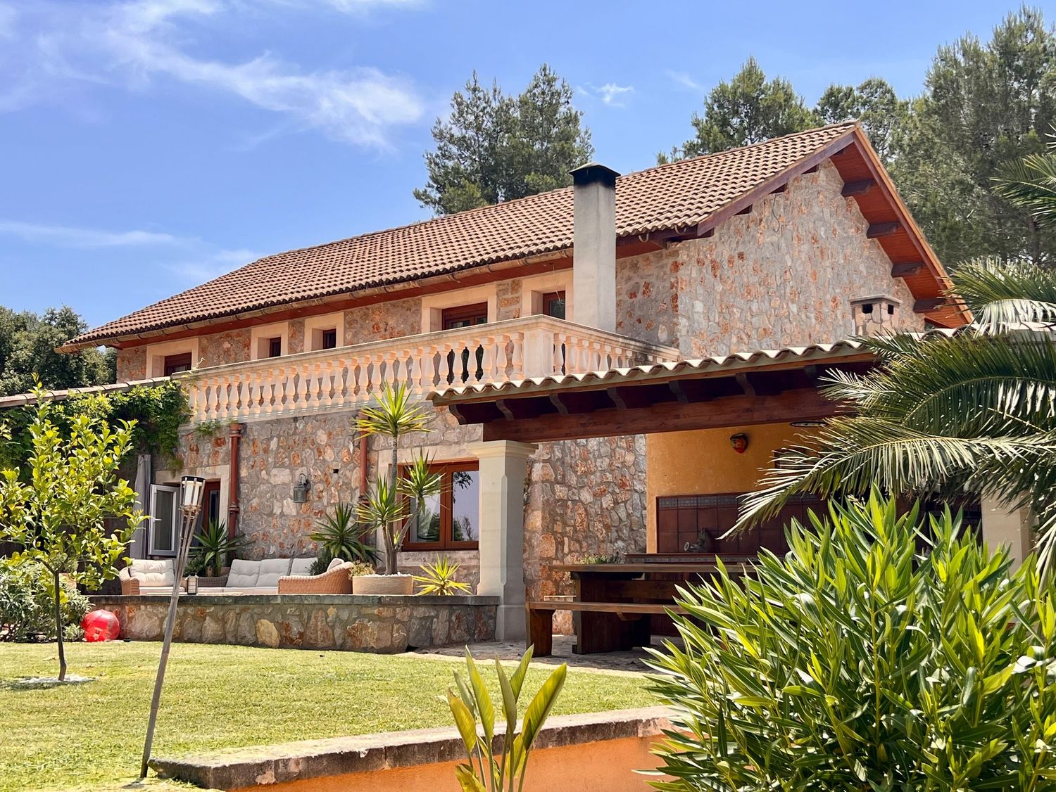 Mediterranean style villa with stone facade, terracotta roof, balcony and lush garden features in sunny outdoor setting.