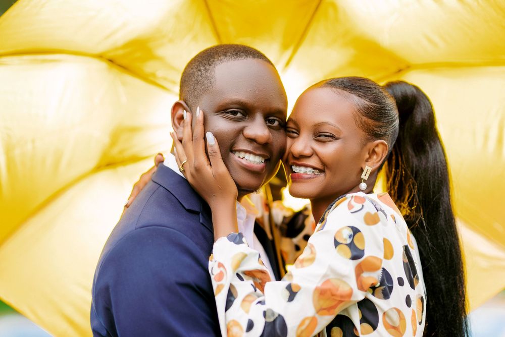 Couple sharing intimate moments under a yellow umbrella during a photo session.
