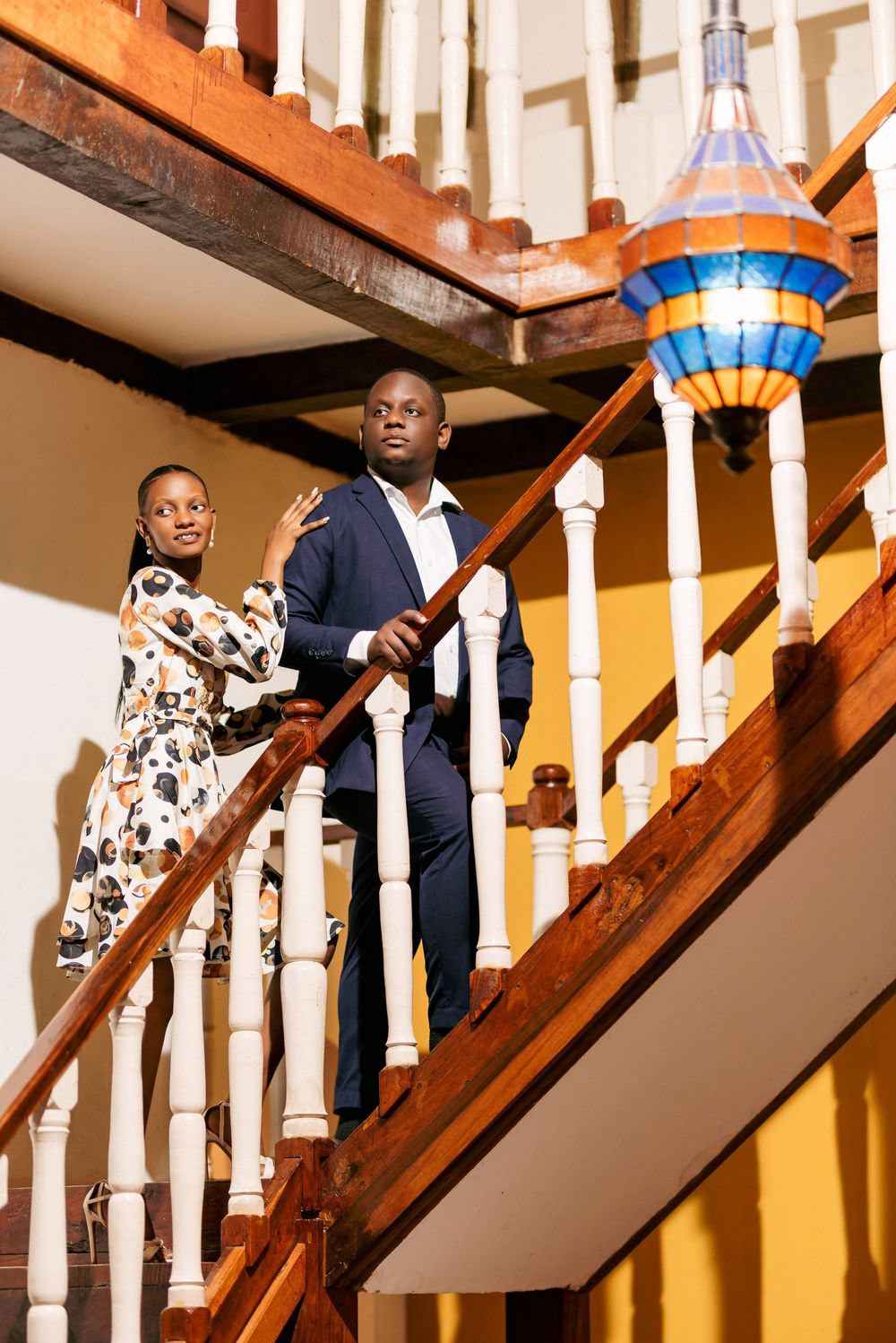 People descending a wooden staircase with decorative railings and colorful stained glass lighting.