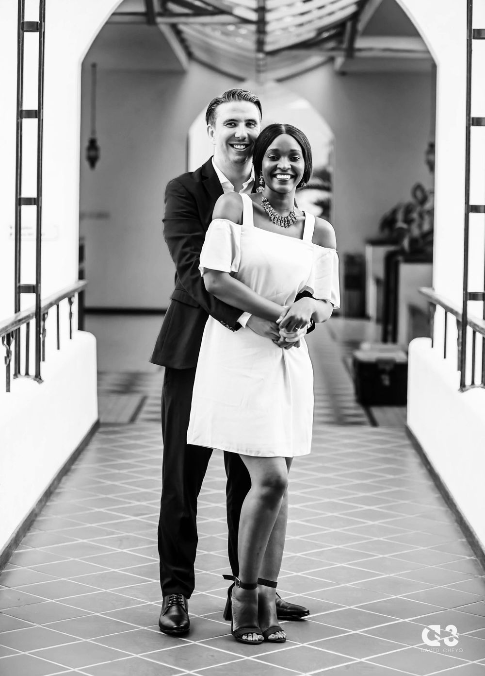 Black and white engagement portrait in elegant hallway with architectural details.