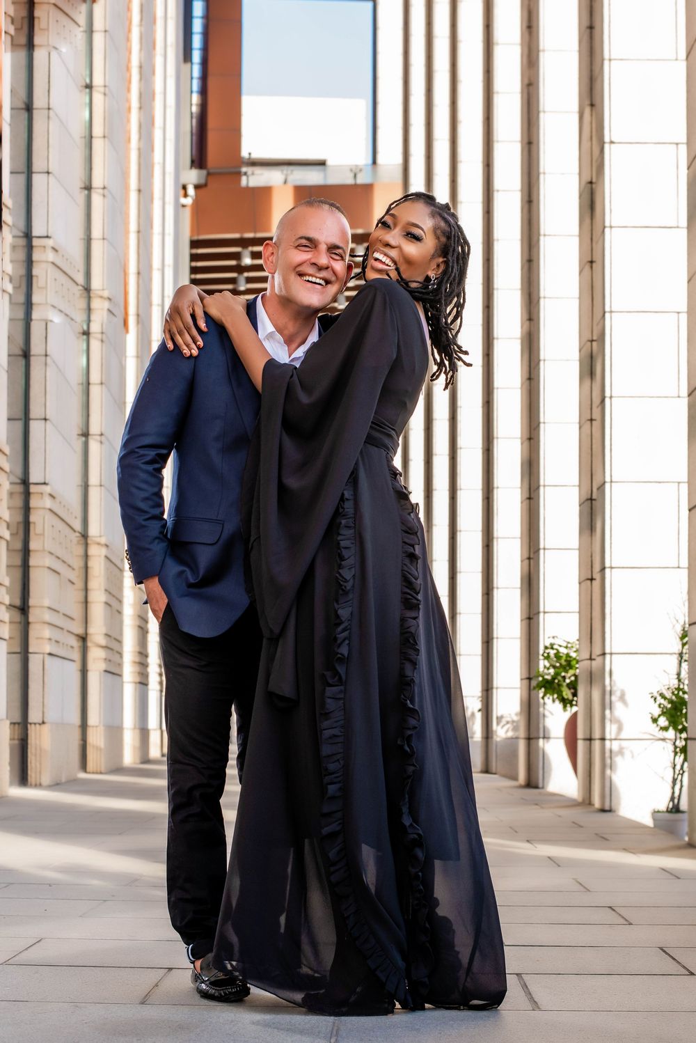 Stylish couple embraces between modern columns in formal attire.