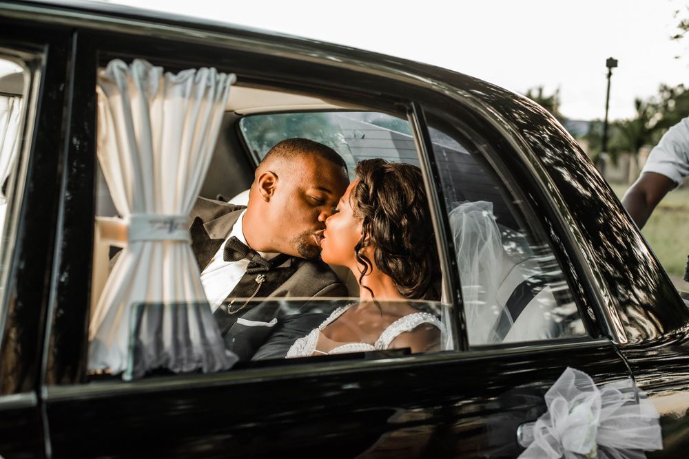 Romantic wedding moment captured through vintage car window during sunset.