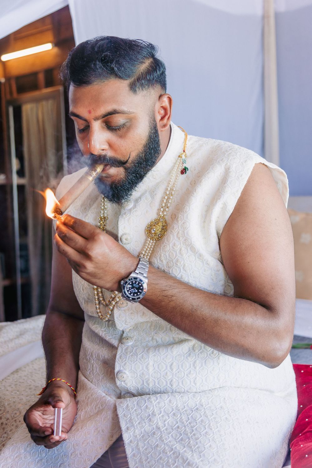 Person in white traditional attire lighting something while wearing a luxury watch.
