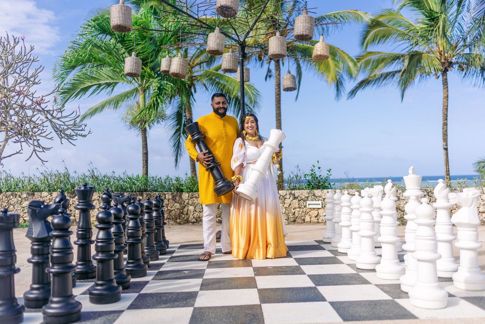 Couple stands on outdoor chess board with tropical palm trees and ocean view.