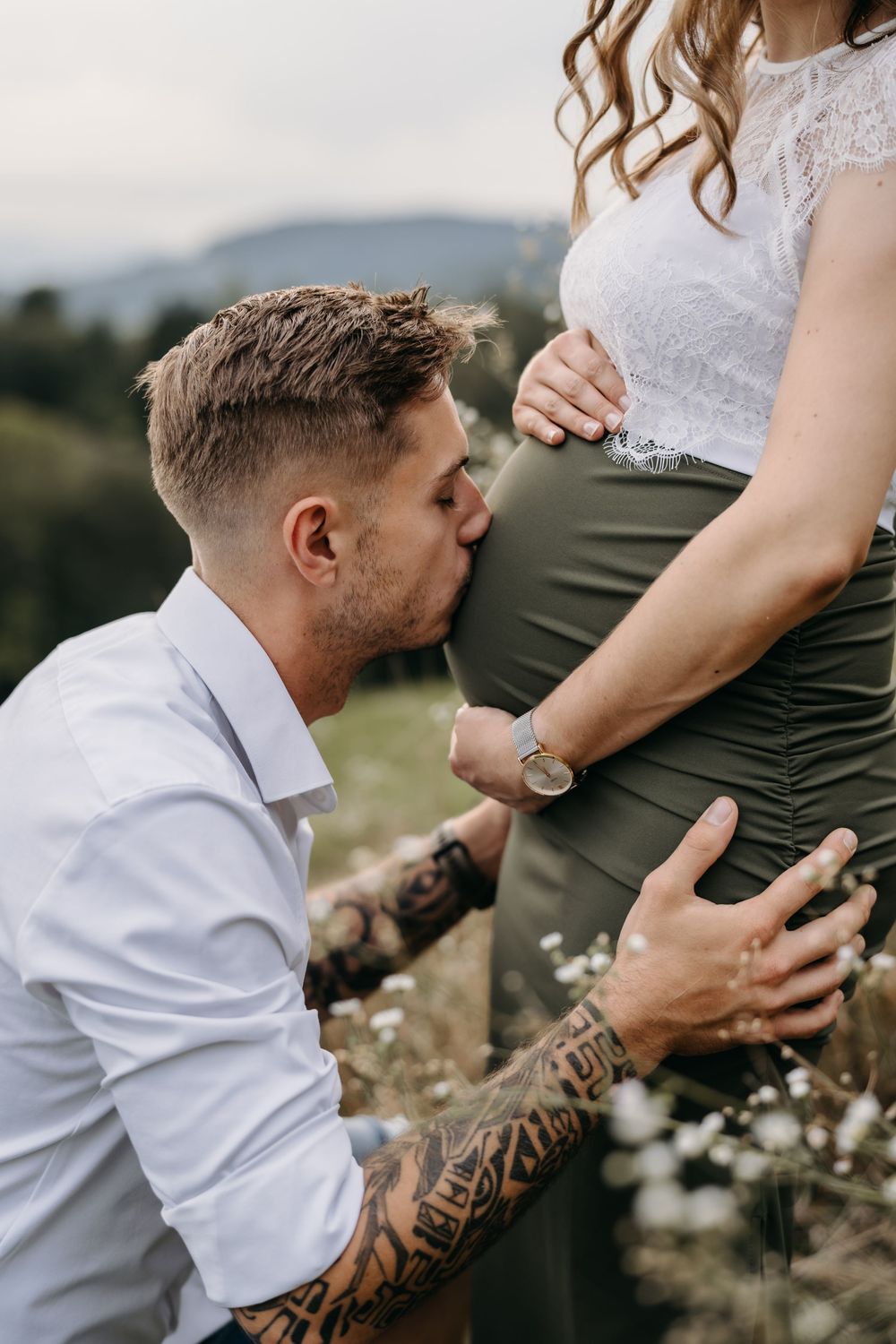 Mann kniet vor seiner schwangeren Partnerin im Freien und küsst liebevoll ihren Babybauch