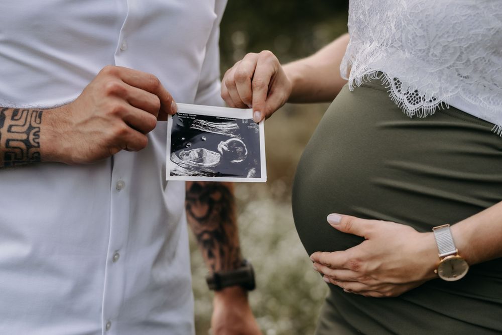 Nahaufnahme eines Paares, das ein Ultraschallbild vor dem Babybauch hält