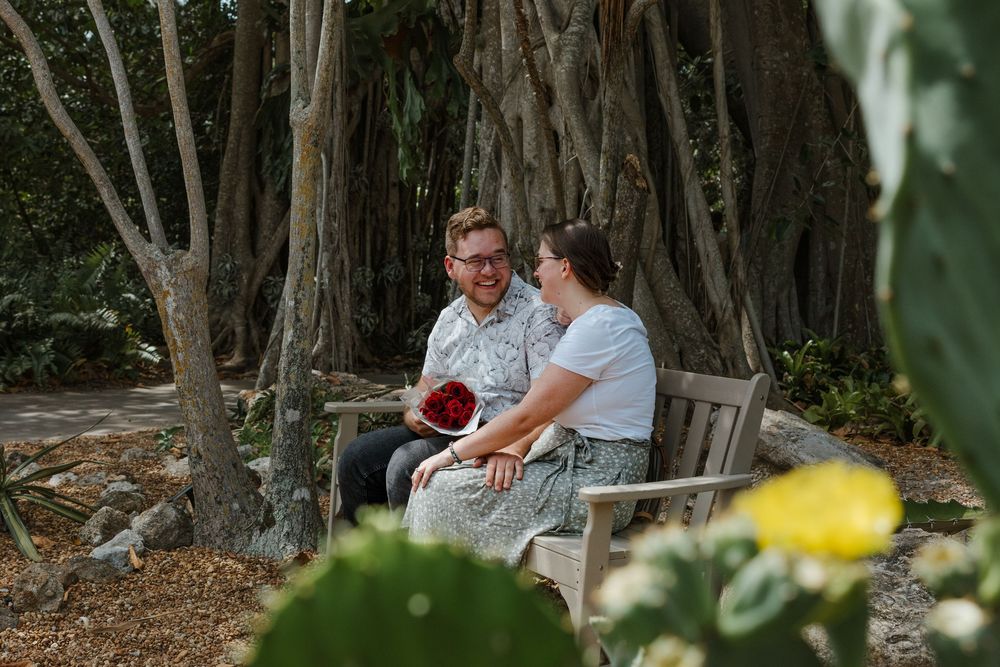 A couple sharing an intimate moment on a rustic bench surrounded by lush garden foliage.