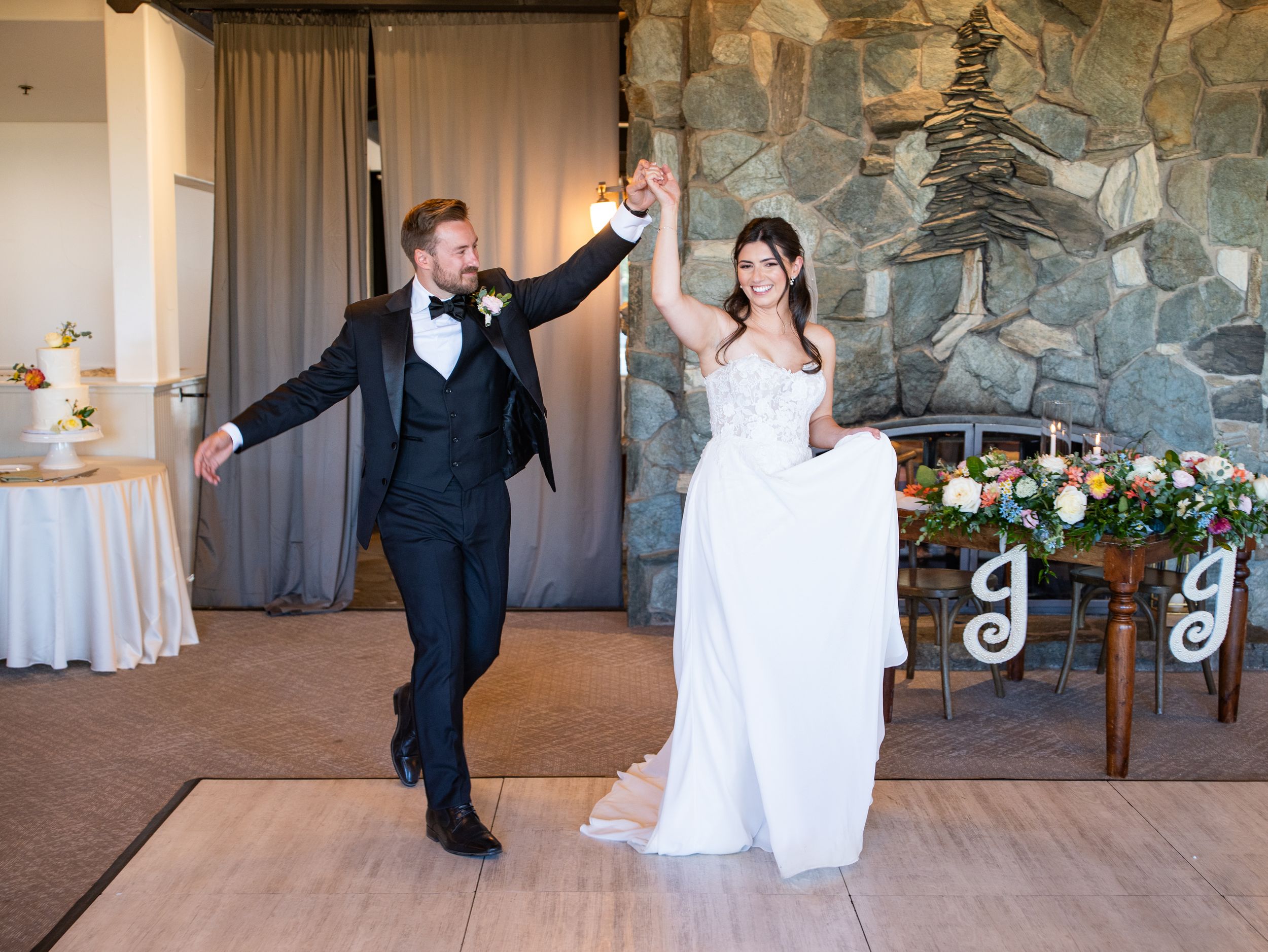 A joyful couple dances together during their first dance at a wedding reception with stone walls and floral decor.