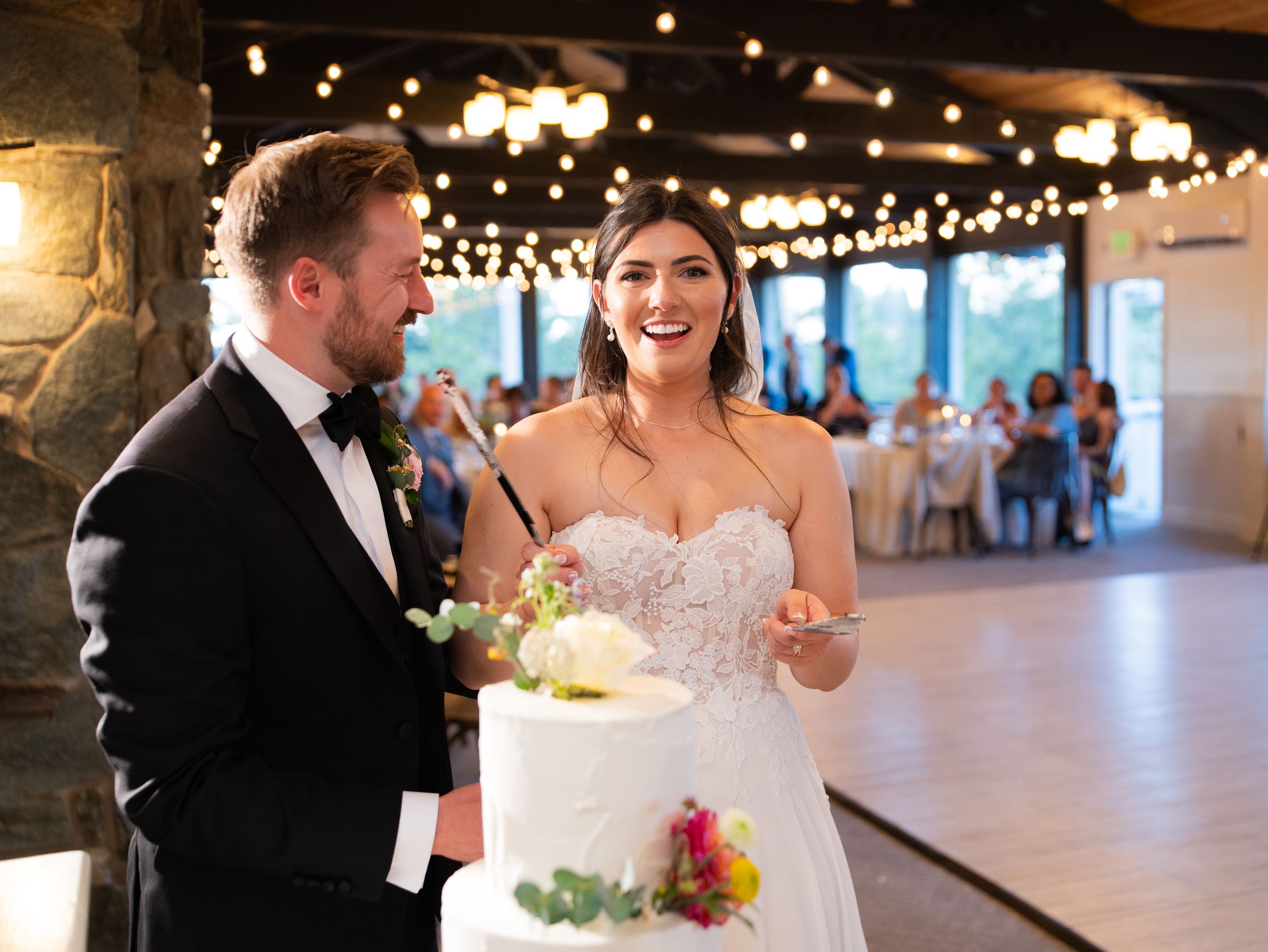 A joyful moment at a wedding reception as newlyweds share a laugh while standing next to their white wedding cake.