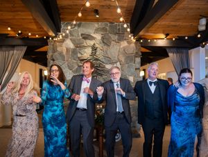People in formal attire enjoying candid group dance moments at an indoor wedding reception with wooden ceiling and lighting.