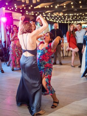 Dancers move energetically on a dance floor under string lights and purple lighting at a festive indoor celebration.