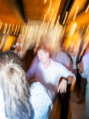 Motion-blurred photo of dancing at a reception shows golden lighting and people moving in a festive atmosphere.