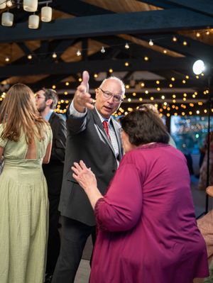 Guests dancing together beneath a tent with twinkling string lights at an evening celebration.