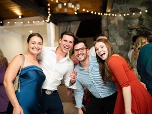 Wedding guests enjoying themselves on the dance floor with festive string lights overhead in an indoor venue.
