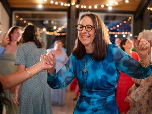 A person in a blue tie-dye dress dances joyfully at a party with string lights in the background.