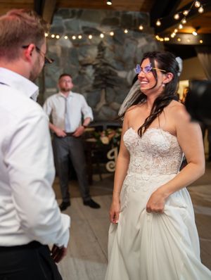 A bride in a strapless lace wedding dress laughs joyfully during a reception under string lights.