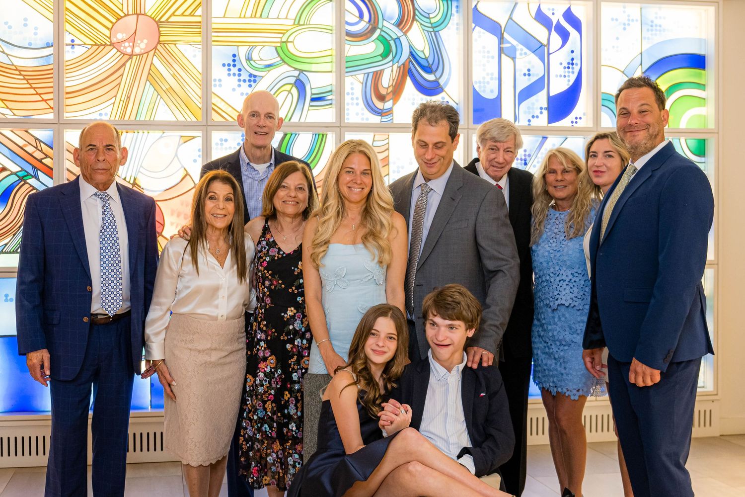 A group stands together smiling for a formal photo in front of a colorful stained glass window with musical notes.