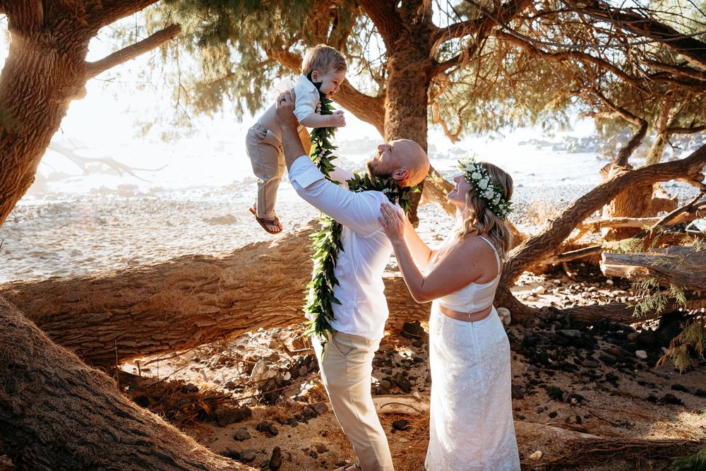 Family celebrating a joyful moment together under giant pine trees on a sunny beach day.
