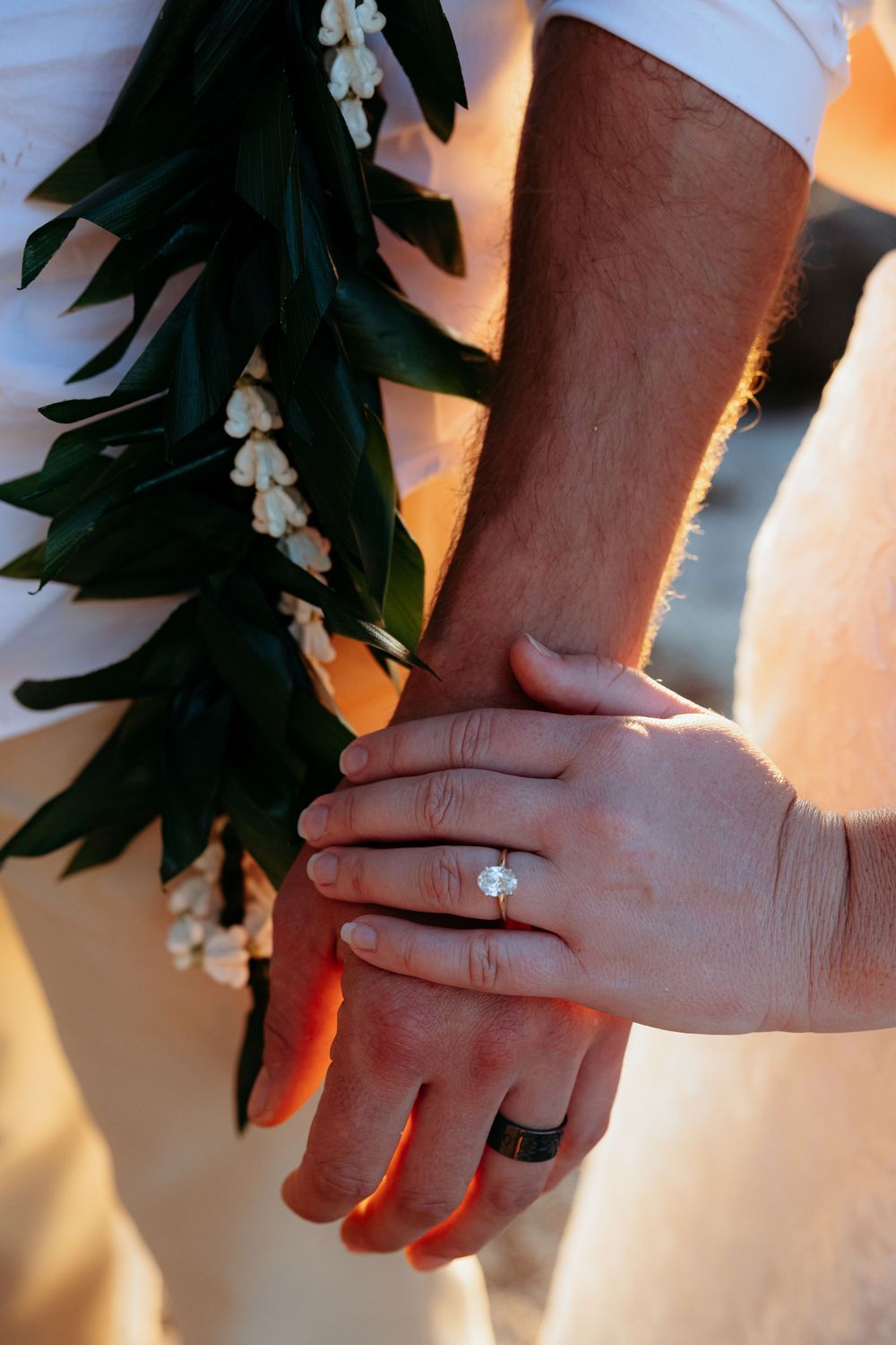 Close-up of hands wearing wedding rings with delicate white flowers and greenery in the background.
