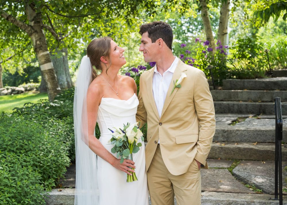 A couple shares romantic moments in a lush garden setting wearing wedding attire with a tan suit and white dress.