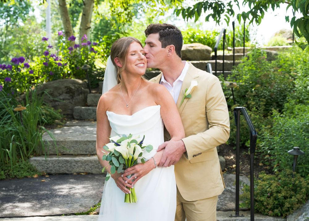 A couple shares a romantic moment in a lush garden setting during a wedding ceremony, with the bride holding a white bouquet.