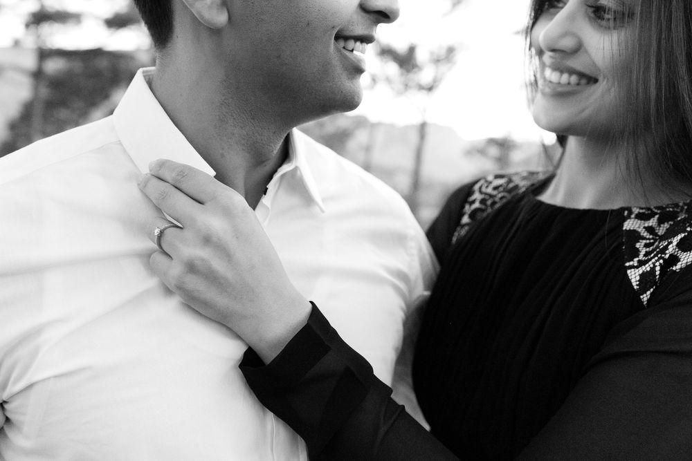A romantic black and white photo of a couple laughing together, with her hand resting on his white shirt collar.