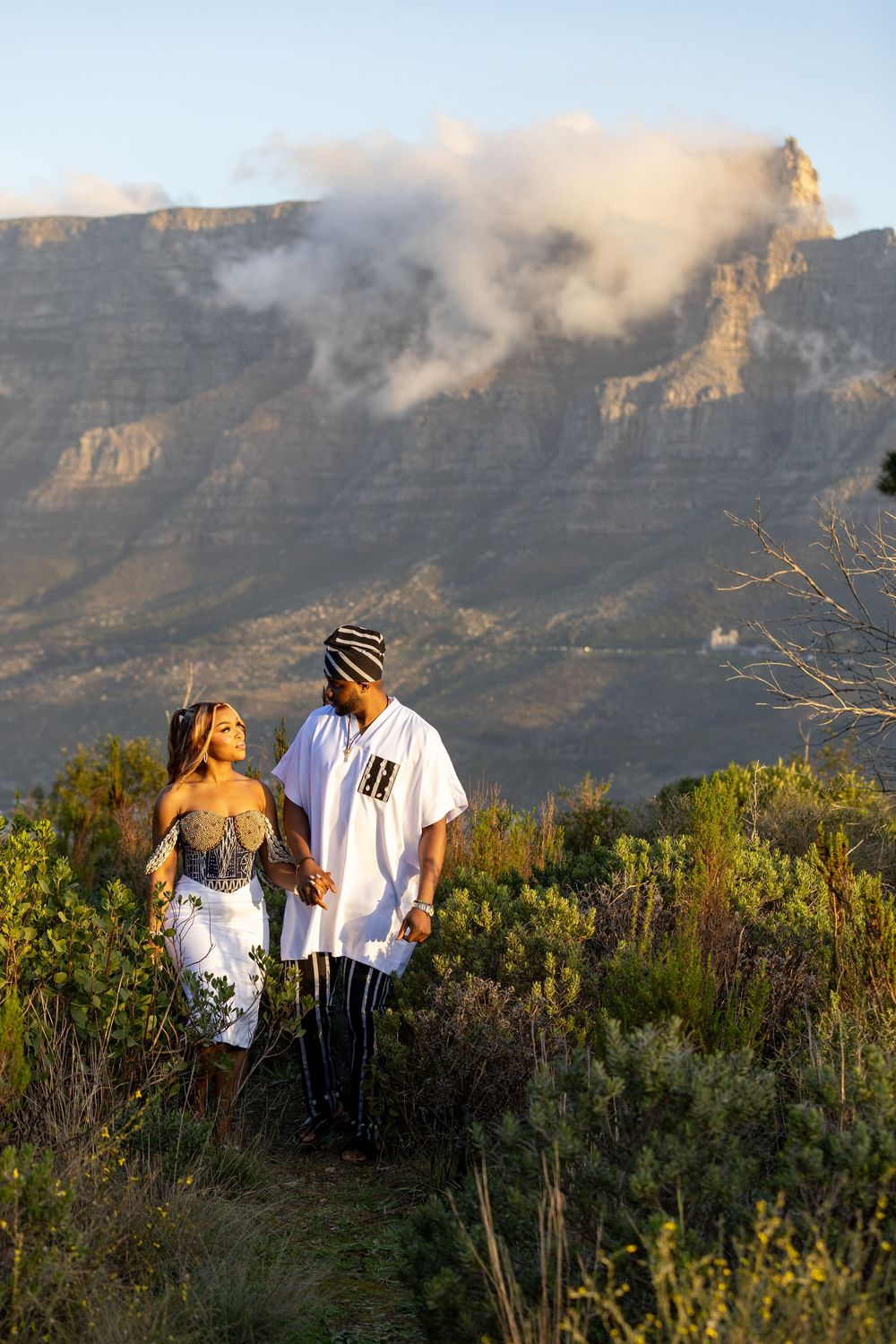 Two people enjoy a scenic walk against the dramatic backdrop of Table Mountain with low clouds in Cape Town, South Africa.